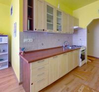 A kitchen in a 2-room apartment with a wooden decor floor and yellow walls.