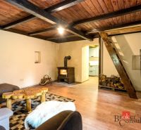 The interior of a cottage with a wooden beam ceiling, a stove, and a floor with a wooden decor.