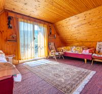 A room in a cabin with wooden paneling, a bed, an armchair, and a carpet on the floor.