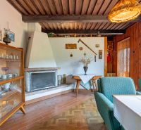 Interior of a cabin with a fireplace, display cabinet, green armchairs, and a wooden-patterned floor.