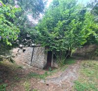 A family house in Svodín with a rock wall, a stone fence, and green trees in the garden.