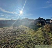 A garden in sunny Tvrdošovce by a family house, fencing, grass, and a blue sky.