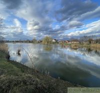 A calm water surface with family houses in Tvrdošovce and a dramatic sky.