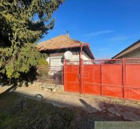 Red gate and fence with a family house in Tvrdošovce, surrounded by greenery.