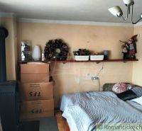 A room with a bed, a shelf, cardboard boxes, and a stove in a family house.