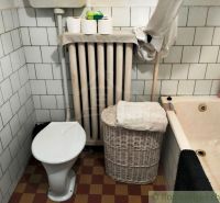 A bathroom in a family house with a bathtub, toilet, radiator, and storage basket.