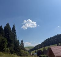 Recreational plots in Litmanová with a forest, road, and wooden cottages under the blue sky.