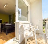A balcony with white plastic chairs, view from a studio apartment, partially showing the interior.