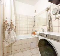 A bathroom with a washing machine, bathtub, and tiles in a studio apartment.