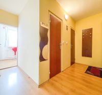 A hallway in a one-room apartment with a floor and light walls, entrance to the room with a red chair.