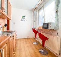 A kitchen in a one-room apartment with a wood-patterned floor and red chairs.