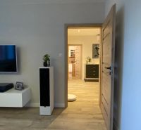 Living room in a three-room apartment with a wooden decor floor and a TV on the wall.