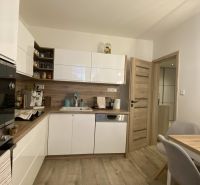 A kitchen with white cabinets, wooden decor, and a dining table in a 3-room apartment.