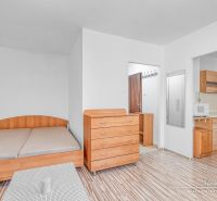 A studio apartment with a bed, a dresser, and a kitchenette with a wooden decor floor.