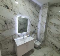 Bathroom in a holiday apartment with marble decor and a mirror with LED backlighting.