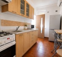 A kitchen in a 2-room apartment with wooden cabinets, a stove, and a dining table.