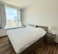 A room with a large window, a bed, and a floor with a wooden decor in a 3-room apartment.