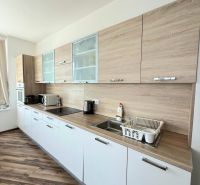 A kitchen unit with white cabinets and a wooden decor floor in a 3-room apartment.