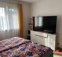 Bedroom in a family house with TV, floral bed linens, yellow curtains, window.