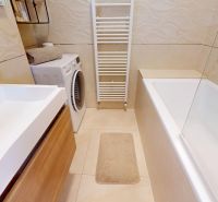 A bathroom with a bathtub, washing machine, white tiles, and a cabinet in a 3-room apartment.