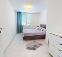 A bright bedroom with wood-patterned flooring, a double bed, and a white dresser in a three-room apartment.
