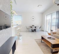 Living room in a three-room apartment with a wooden decor floor, a sofa, and a dining table.