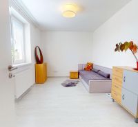 A room in a 3-room apartment with a sofa, a chest of drawers, and a floor with a wooden decor.