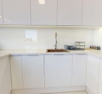 A kitchen unit in a 3-room apartment with white cabinets and a green climbing plant.