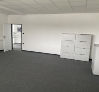 A white office with a dark gray carpet, light furniture, and open doors.