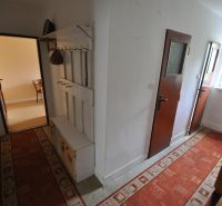 A narrow hallway in a 2-room apartment, with a red carpet and a coat rack on the wall.