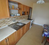 A kitchen in a 2-room apartment with wooden cabinets and tiled backsplash.