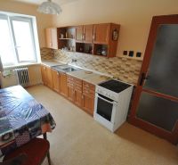 The kitchen of a 2-room apartment with a dining table, kitchen unit, and electric stove.