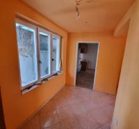 An orange-painted hallway with windows and tiles, leading to another room in a family house.