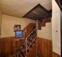 Interior of a family house with a metal staircase, worn-out walls, and a window with wallpaper.
