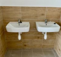 Two sinks on a wall with wood decor tiles in warehouses and halls.