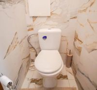 A toilet in a bathroom with marble tiles in a 2-room apartment.