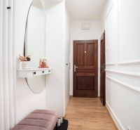 The hallway of a 2-room apartment with a wooden decor floor and a mirror on the wall.