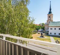 View from the balcony in Nové Zámky, near a 2-room apartment, with a church and greenery.