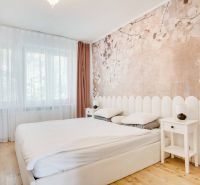 Bedroom in a two-room apartment with a wooden decor floor and subtle wallpaper.