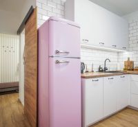 A kitchen in a 2-room apartment with a retro pink refrigerator and a wooden decor floor.