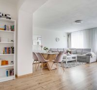 Living room in a two-room apartment with a wooden decor floor, light seating, and a bookshelf.