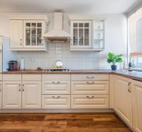 A kitchen with beige cabinets, wood-patterned flooring, a plant, and appliances in a 4-room apartment.