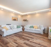 Living room in a 4-room apartment with white sofas and a floor with a wooden decor.