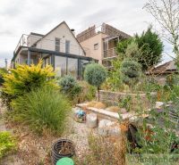 A cottage in Senec with a garden, green plants, and a terrace on the upper floor.
