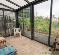 A cottage with a glass-enclosed terrace and a floor with a wooden decor, overlooking the garden.