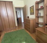 A bedroom in a two-room apartment with wooden furniture, a green carpet, and a floor with a wooden decor.
