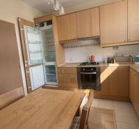 A kitchen in a 2-room apartment with built-in appliances, wooden cabinets, and a floor with a wooden decor.