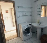 A bathroom in a 2-room apartment with a mirror, sink, and washing machine on the tiles.