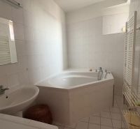 A bathroom with a corner bathtub and white tiles in a two-room apartment.