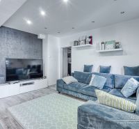 Living room in a 3-room apartment with a large TV, comfortable sofa, and wooden decor flooring.